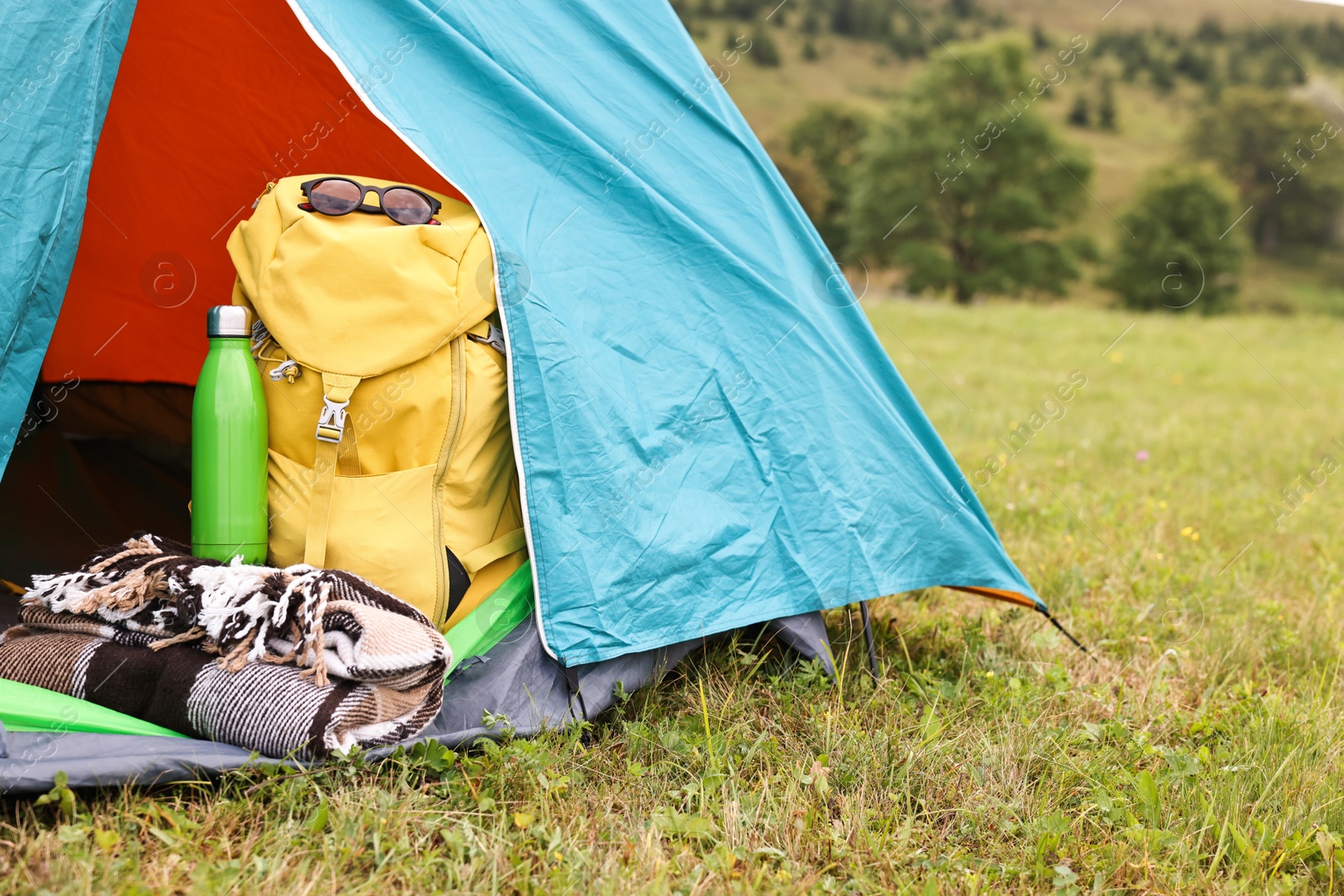 Photo of Tent, backpack, blanket and thermos on green grass in mountains, space for text