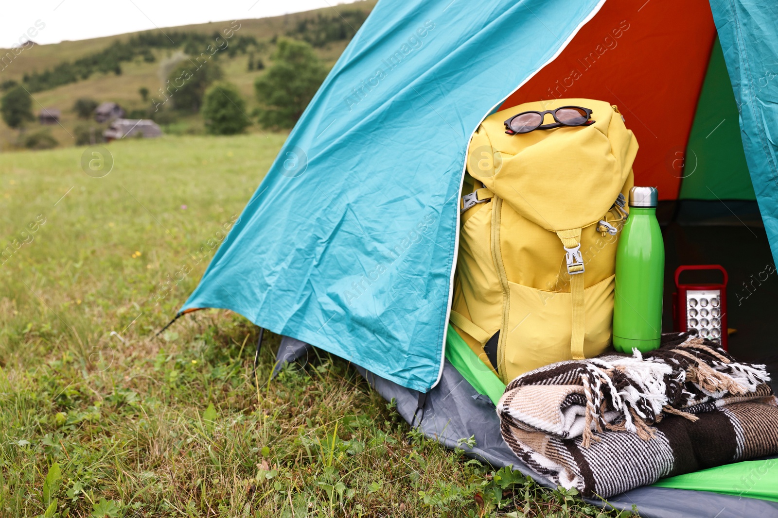 Photo of Tent, backpack, blanket and thermos on green grass in mountains, space for text