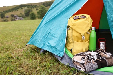 Photo of Tent, backpack, blanket and thermos on green grass in mountains, space for text