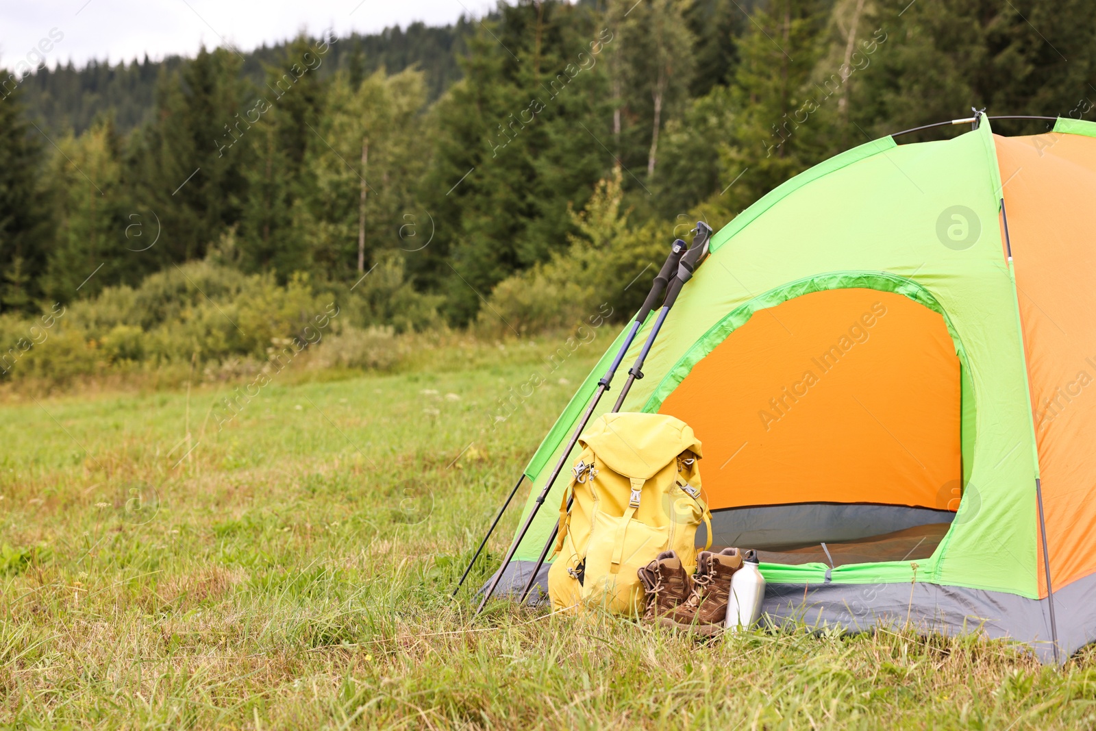 Photo of Tent, backpack, trekking poles and thermos on green grass in mountains, space for text