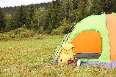 Tent, backpack, trekking poles and thermos on green grass in mountains, space for text