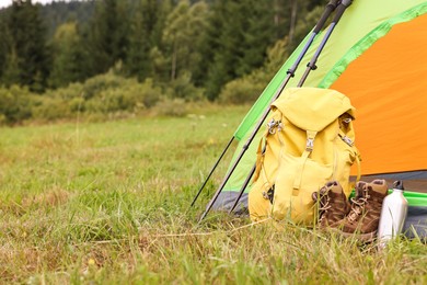 Photo of Tent, backpack, trekking poles and thermos on green grass in mountains, space for text