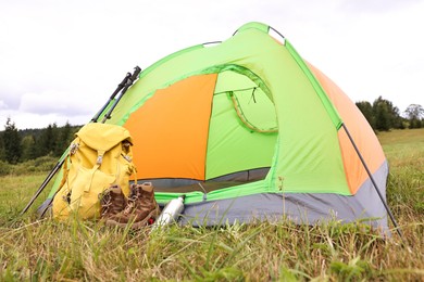 Tent, backpack, trekking poles and thermos on green grass in mountains