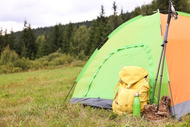 Photo of Tent, backpack, trekking poles and thermos on green grass in mountains, space for text