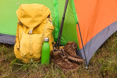 Tent, backpack, trekking poles and thermos on green grass in mountains