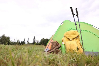 Tent, backpack, trekking poles and thermos on green grass in mountains, space for text