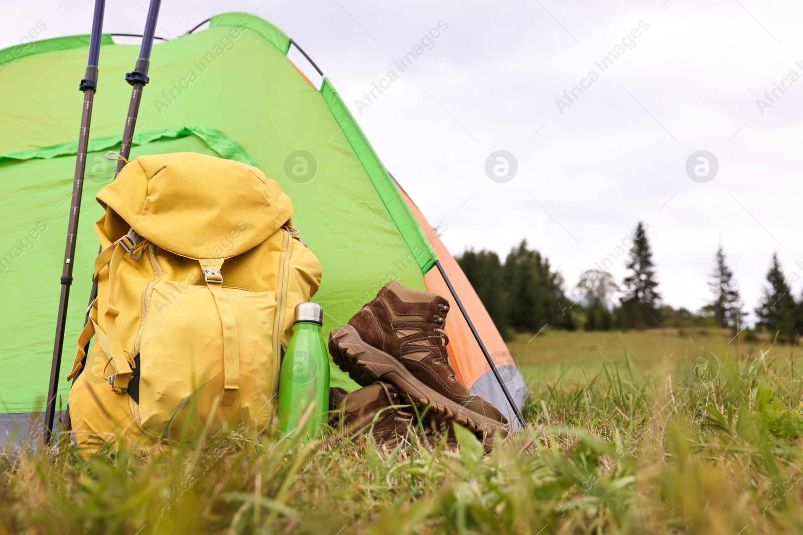 Photo of Tent, backpack, trekking poles and thermos on green grass in mountains, space for text