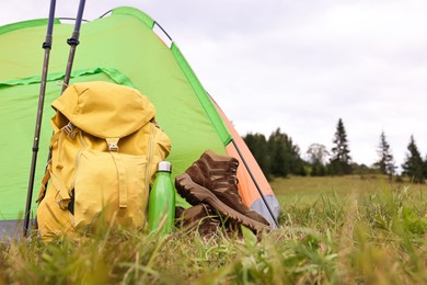 Tent, backpack, trekking poles and thermos on green grass in mountains, space for text