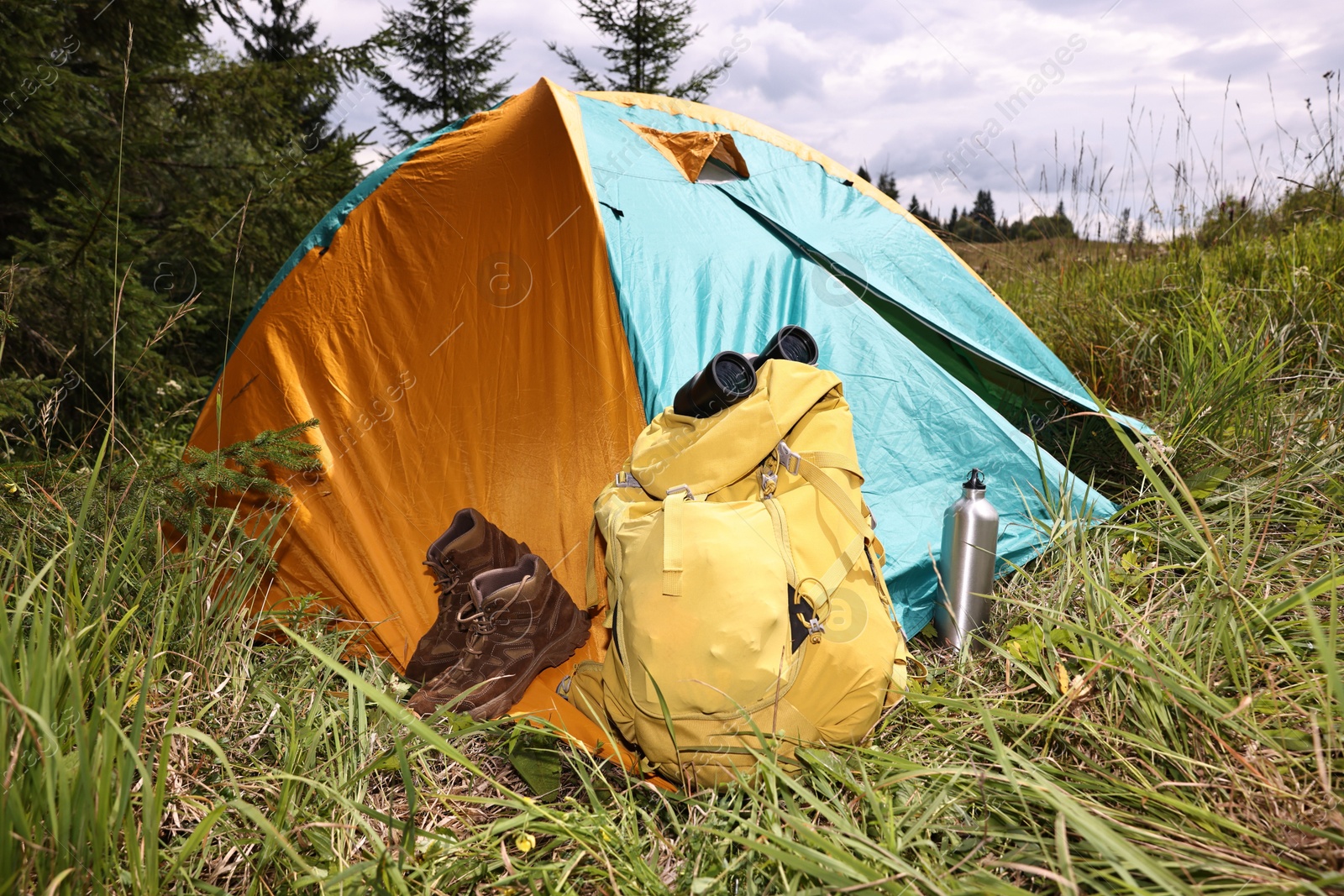 Photo of Tent, backpack, binoculars and shoes on green grass outdoors