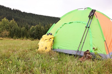 Photo of Tent, backpack and trekking poles on green grass in mountains