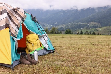 Camping tent and tourist stuff on grass in mountains, space for text