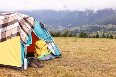 Camping tent and tourist stuff on grass in mountains, space for text