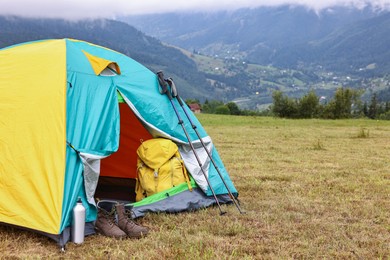 Camping tent and tourist stuff on grass in mountains, space for text