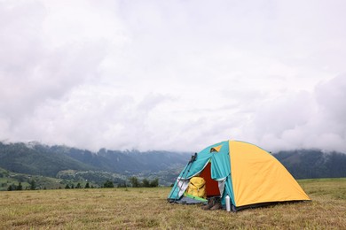 Camping tent and tourist stuff on grass in mountains, space for text