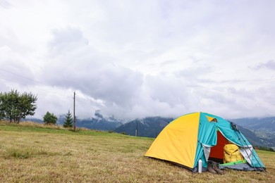 Camping tent and tourist stuff on grass in mountains, space for text