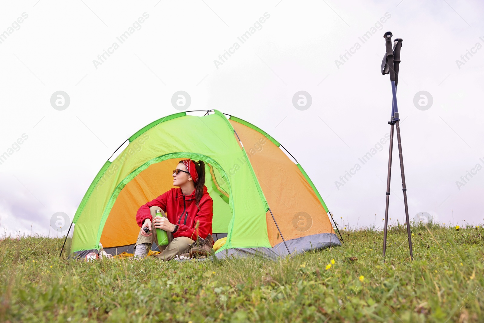 Photo of Young woman with thermo bottle sitting in camping tent on green grass outdoors