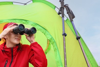 Photo of Young woman looking through binoculars near tent outdoors, low angle view