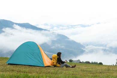 Photo of Young camper with backpack and tent in mountains, space for text