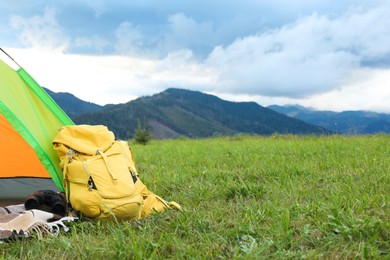 Tent and backpack on green grass in mountains, space for text