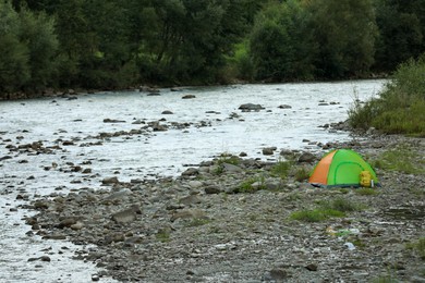 Photo of Camping tent, backpack and thermo bottle on stones near river in mountains