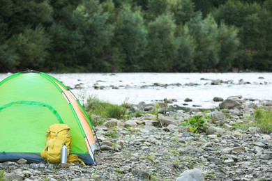 Photo of Camping tent, backpack and thermo bottle on stones near river in mountains