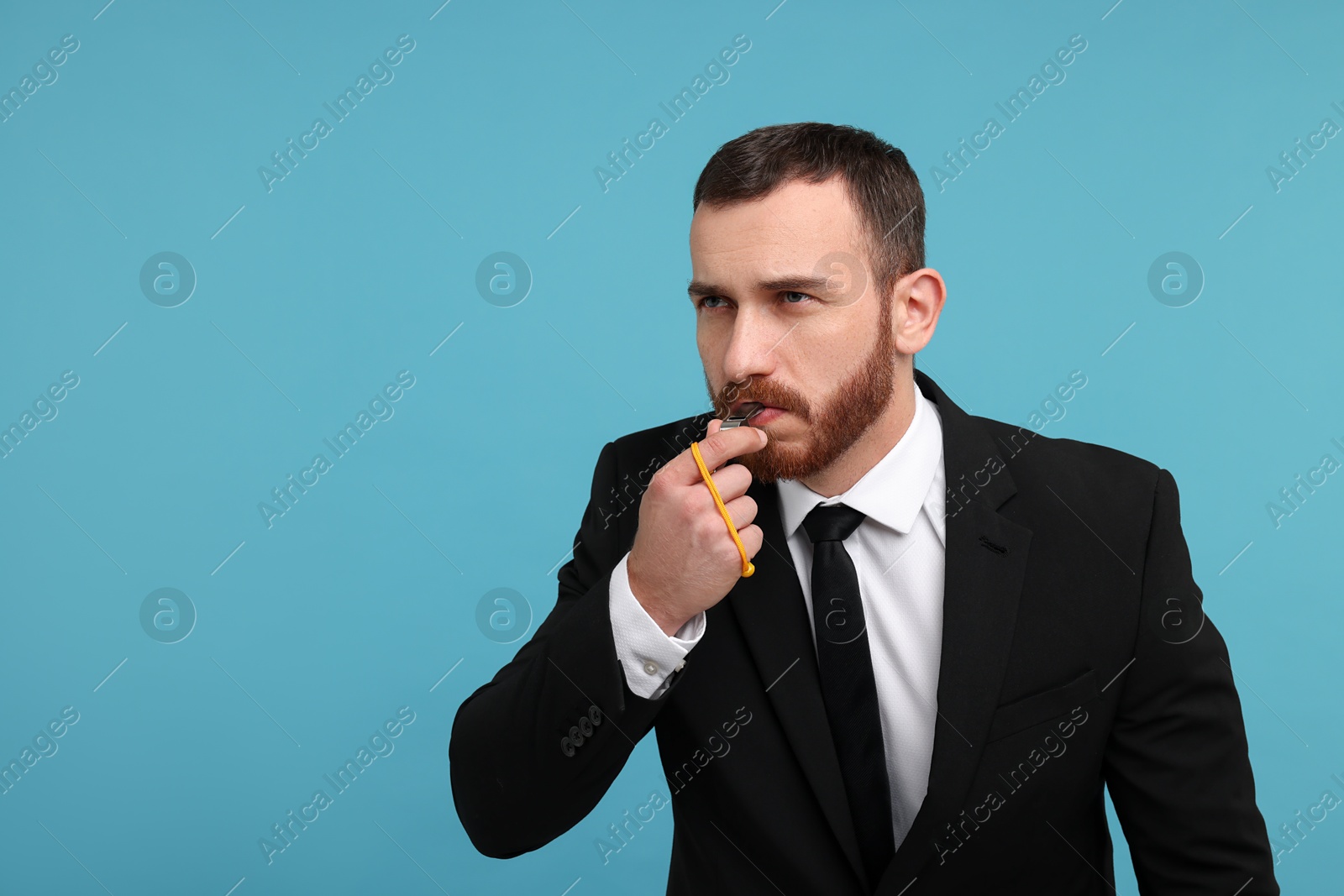 Photo of Young man blowing whistle on light blue background, space for text