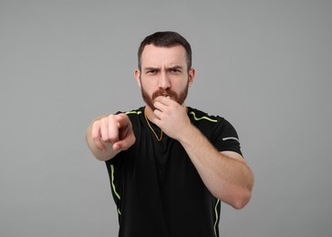 Young man blowing whistle on grey background