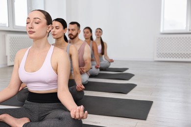 Photo of Group of people meditating on mats in yoga class. Space for text