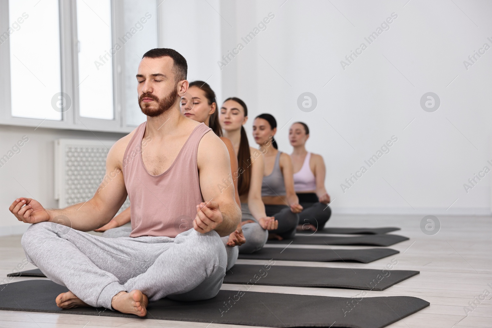 Photo of Group of people meditating on mats in yoga class. Space for text