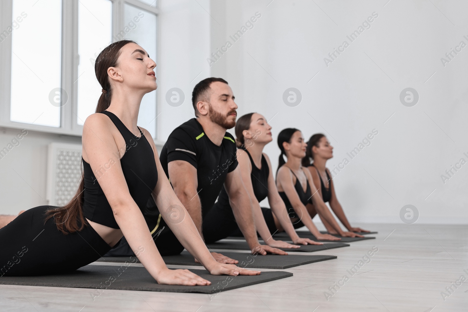 Photo of Group of people practicing yoga on mats in class. Space for text