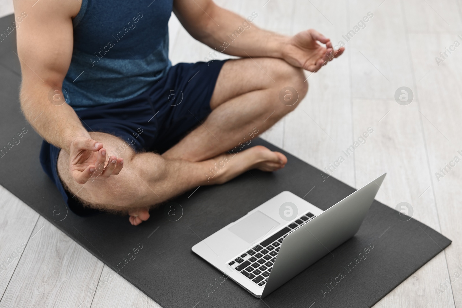 Photo of Man meditating near laptop on yoga mat at home, closeup