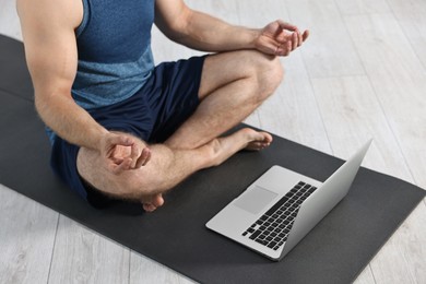 Man meditating near laptop on yoga mat at home, closeup