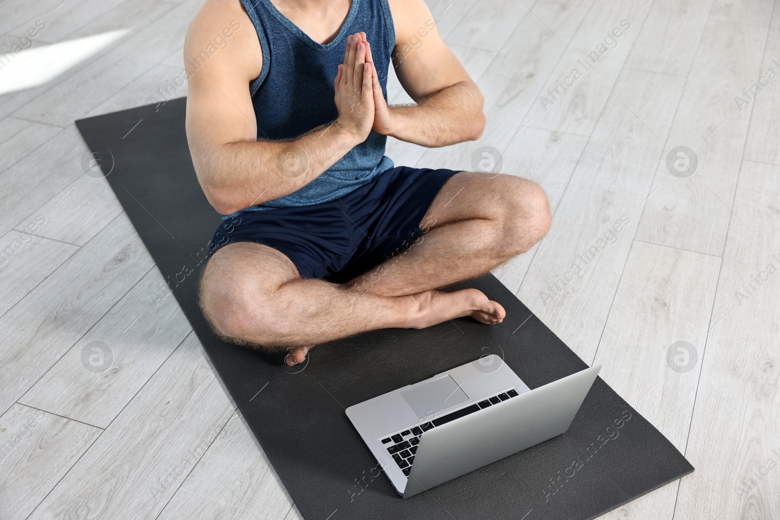 Photo of Man meditating near laptop on yoga mat at home, closeup