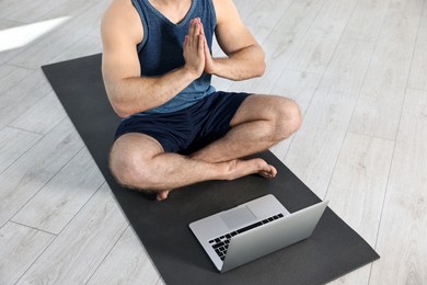 Photo of Man meditating near laptop on yoga mat at home, closeup