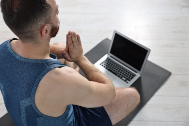 Photo of Man meditating near laptop on yoga mat at home