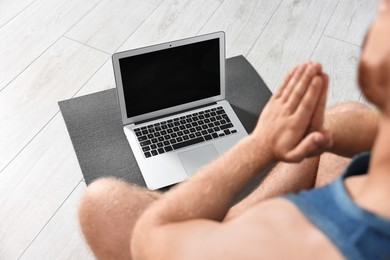 Man meditating near laptop on yoga mat at home, closeup