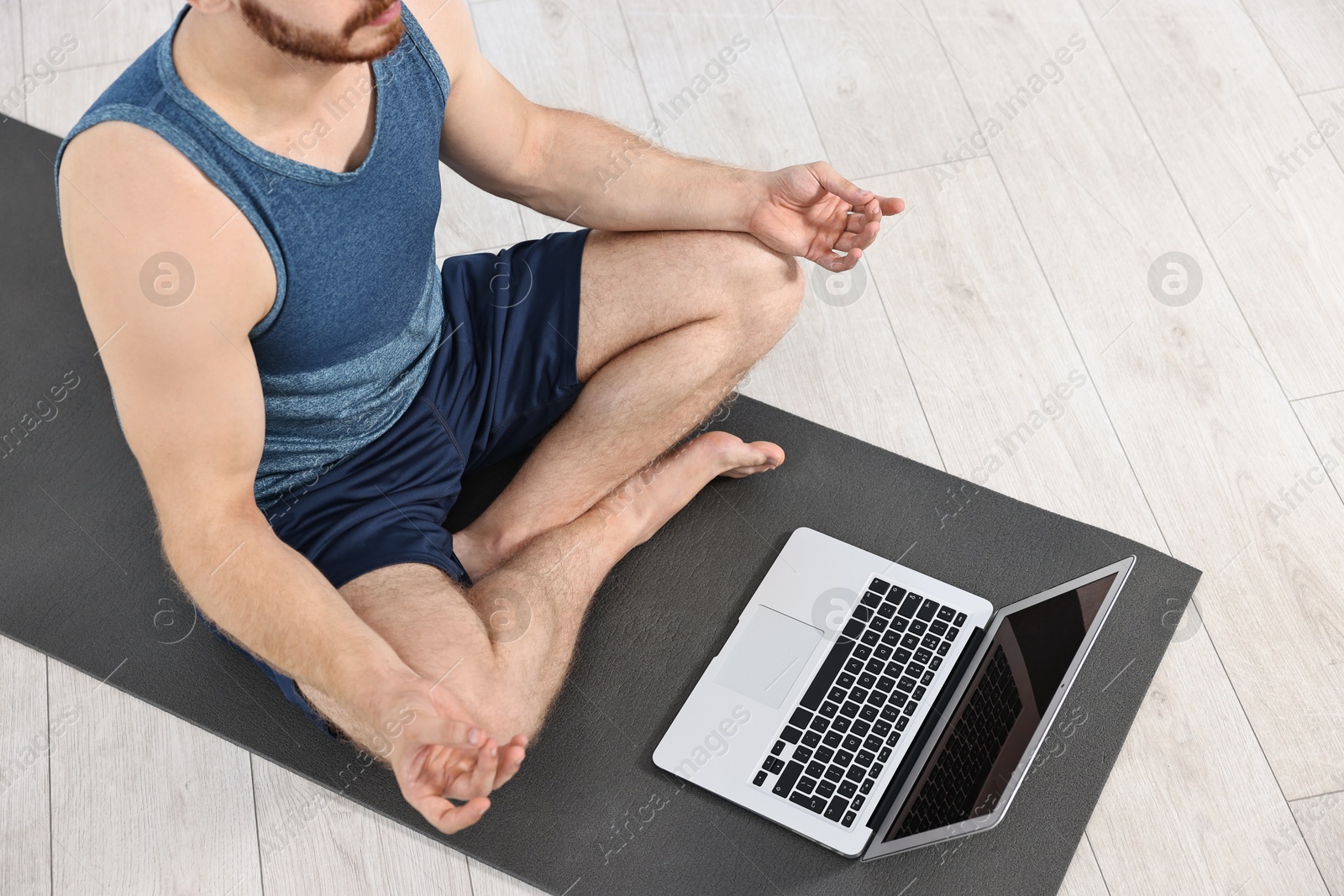 Photo of Man meditating near laptop on yoga mat at home, closeup