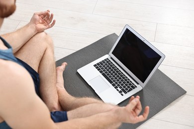 Man meditating near laptop on yoga mat at home, closeup