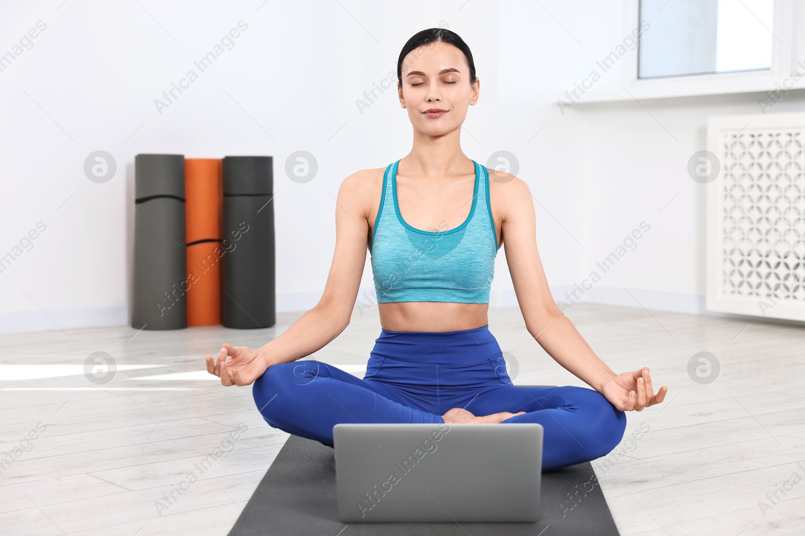 Photo of Woman meditating near laptop on yoga mat at home