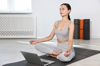 Photo of Woman meditating near laptop on yoga mat at home