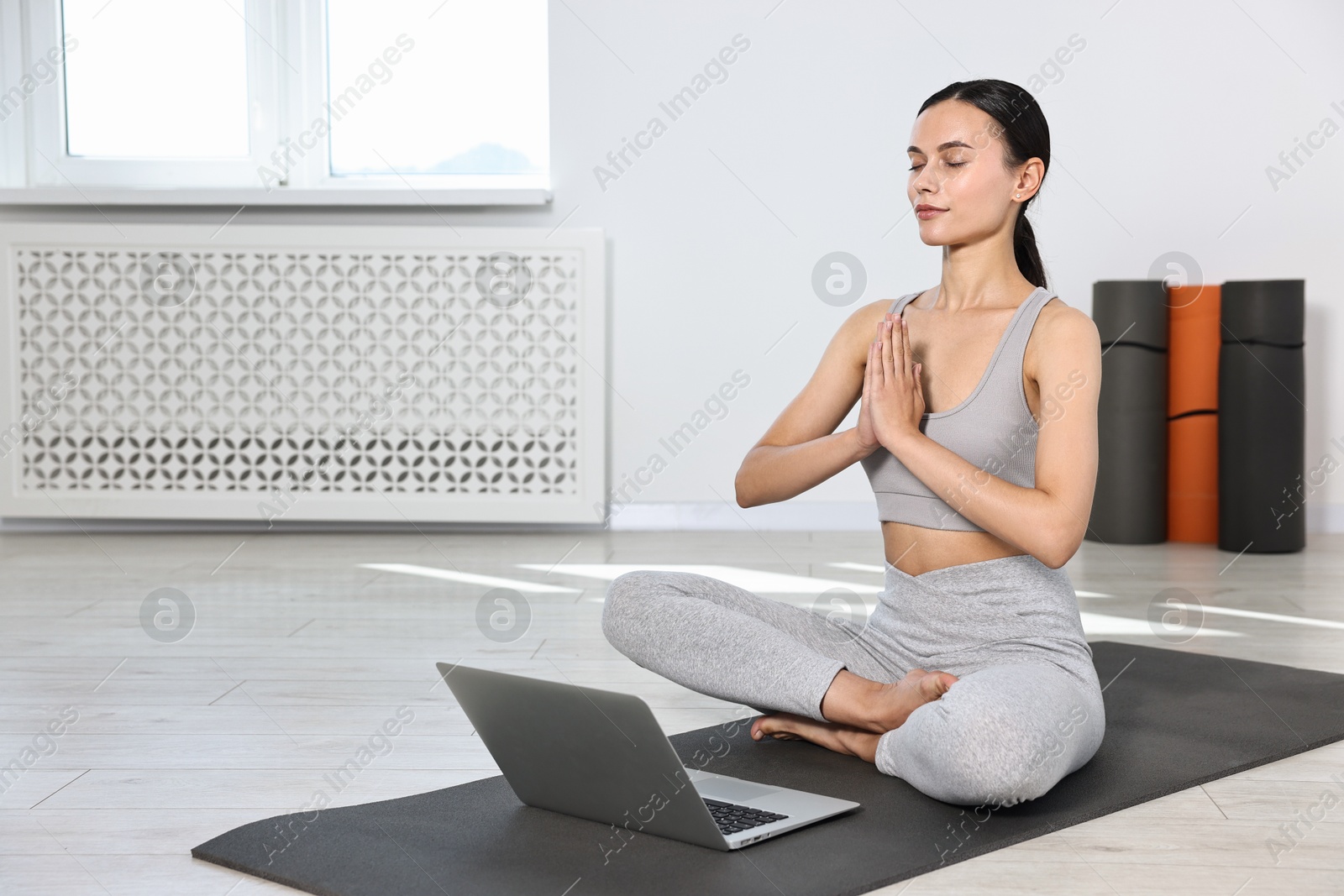 Photo of Woman meditating near laptop on yoga mat at home. Space for text