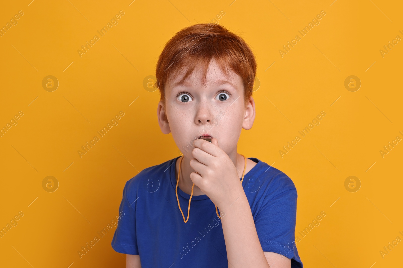 Photo of Little boy blowing whistle on orange background