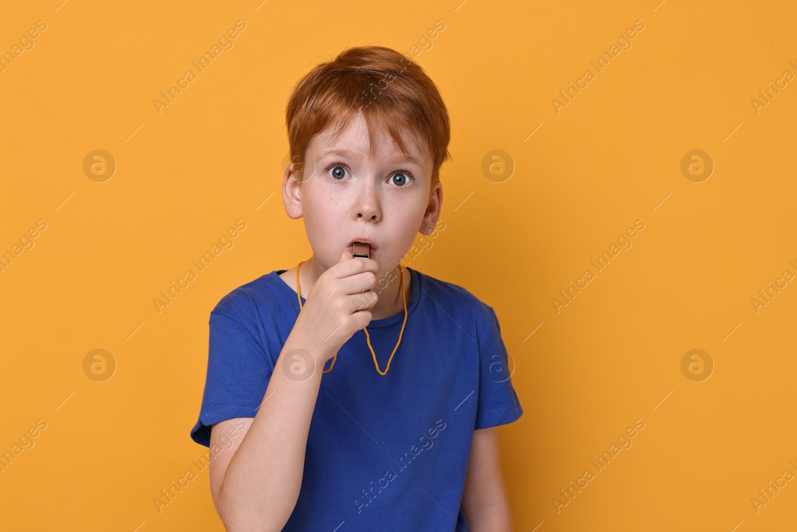 Photo of Little boy blowing whistle on orange background