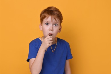 Little boy blowing whistle on orange background