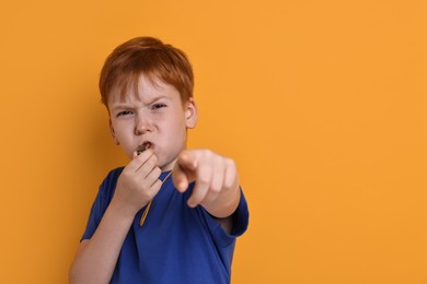 Photo of Little boy blowing whistle on orange background, space for text