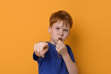 Photo of Little boy blowing whistle on orange background