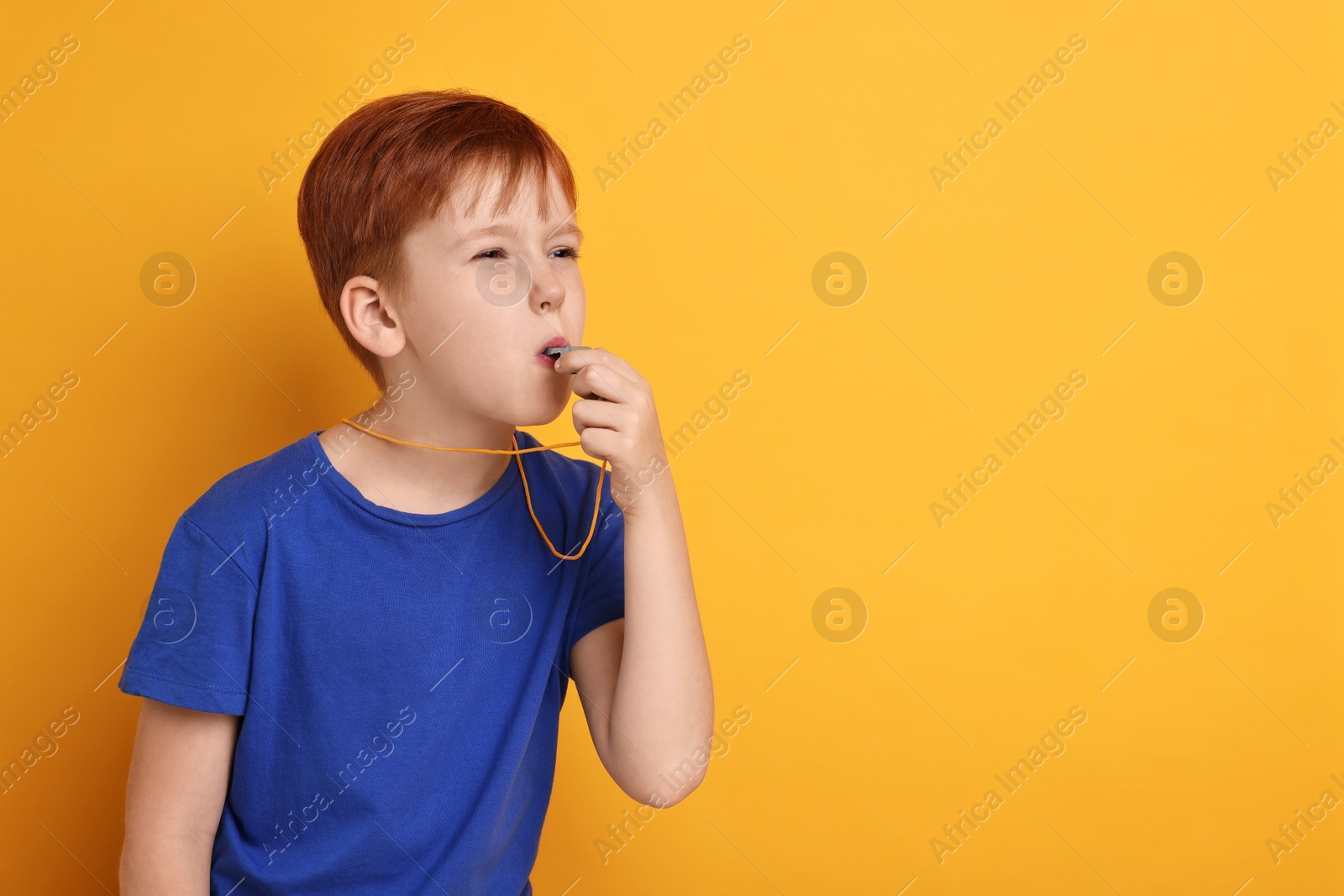 Photo of Little boy blowing whistle on orange background, space for text