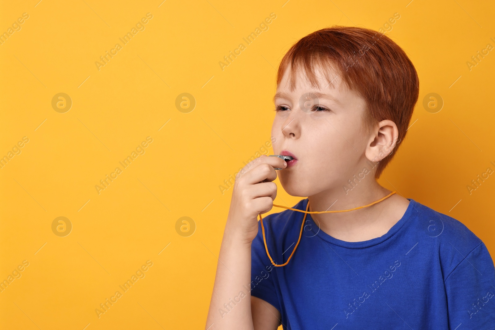 Photo of Little boy blowing whistle on orange background, space for text