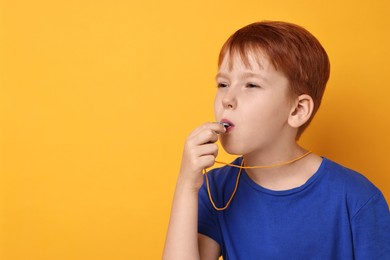 Little boy blowing whistle on orange background, space for text