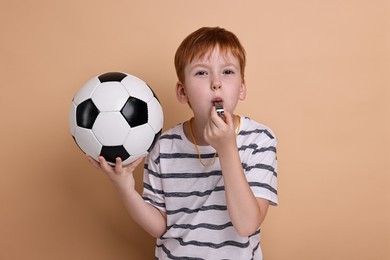 Photo of Little boy with soccer ball blowing whistle on beige background